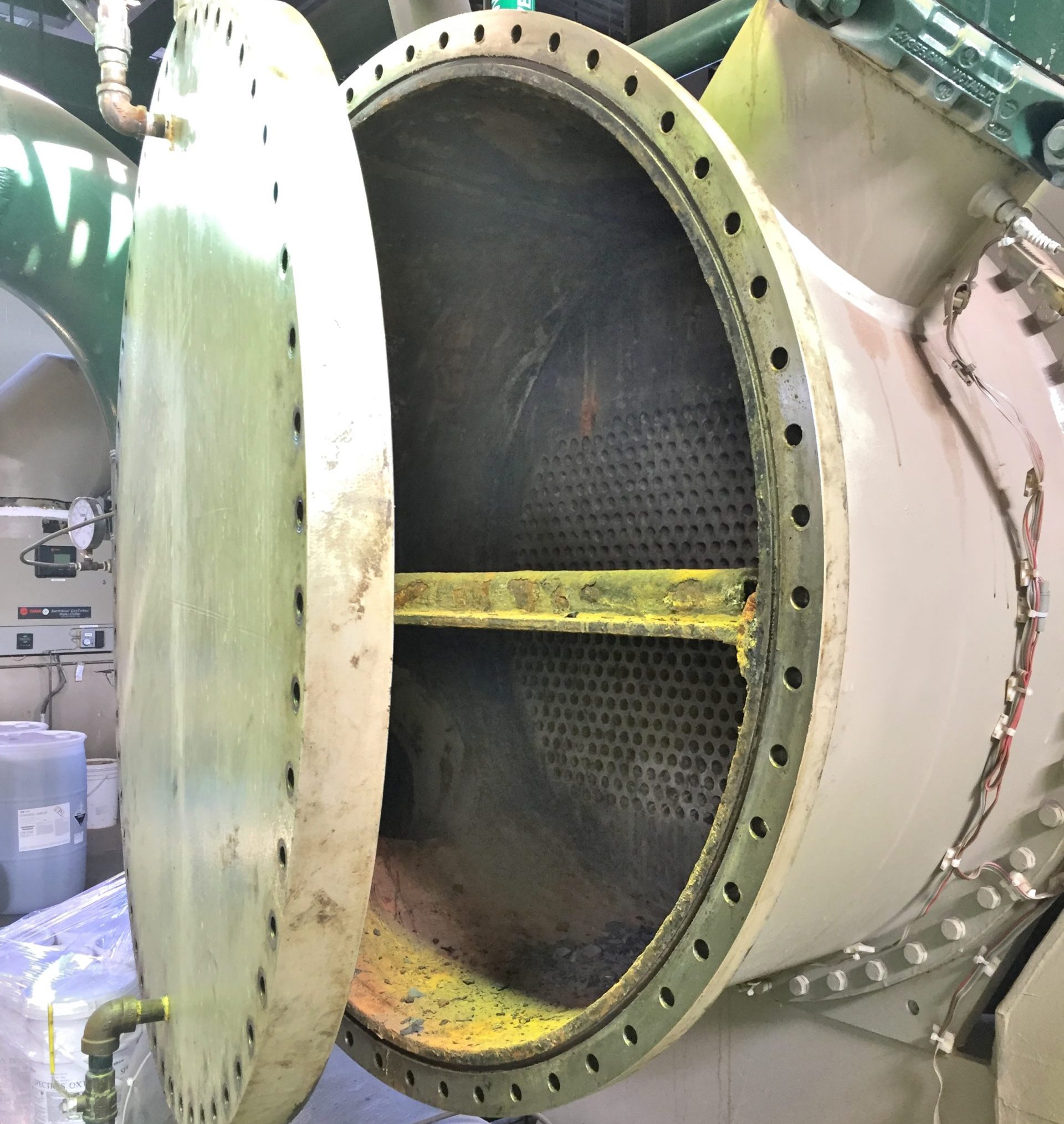 A green shell and tube chiller condenser with the end plate being removed for tube cleaning