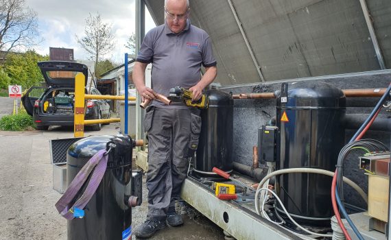 Engineer next to industrial chiller carrying out repair service to compressor