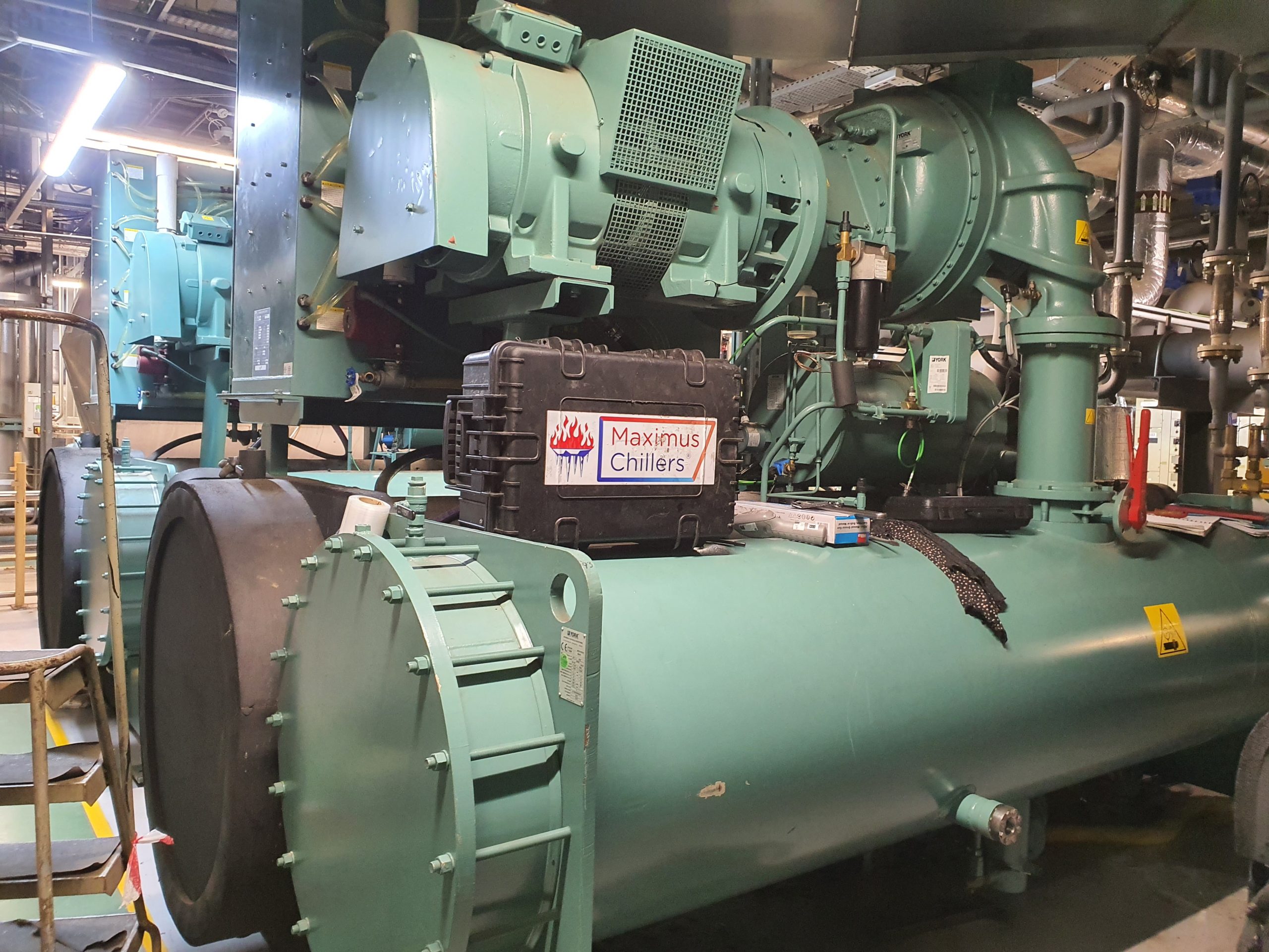 Plant room with row of 3 green centrifugal chillers for service, maintenance and repair